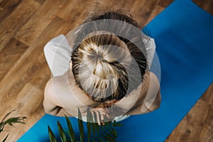 Back view of young woman in sportswear sitting in lotus position while doing yoga at home. Exercises for Back