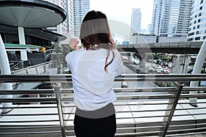 Back view of young woman standing and looking far away in urban city background.