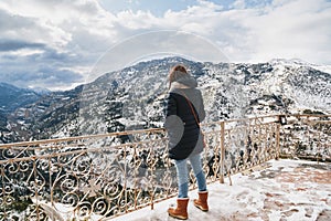 Back view of young woman standing at mountain top observation deck over Vouraikos gorge. Mega Spileon Monastery terrace