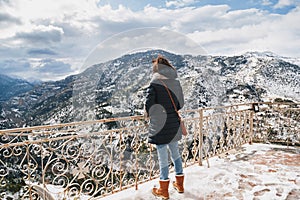 Back view of young woman standing at mountain top observation deck over Vouraikos gorge. Mega Spileon Monastery terrace