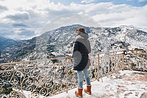 Back view of young woman standing at mountain top observation deck over Vouraikos gorge. Mega Spileon Monastery terrace