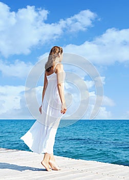 Back view of a young woman standing on a pier. Sea and sky back