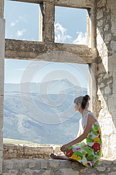 Back view of young woman in sundress looking at view from window