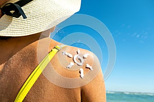 Back view of young woman tanning at the beach with sunscreen cream in sun shape on her shoulder. UV sunburn protection and