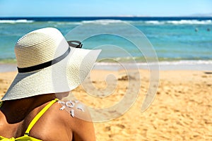 Back view of young woman tanning at the beach with sunscreen cream in sun shape on her shoulder. UV sunburn protection and