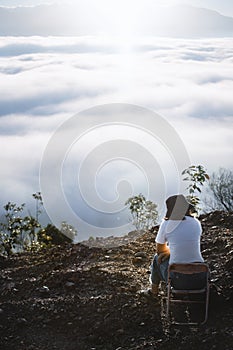 Back view of young woman traveler enjoying sunrise scenery view of fluffy sea fog misty clouds in high mountains