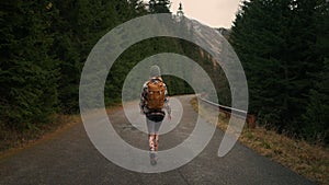 Back view of the young woman traveller walking in middle of empty road in mountains.