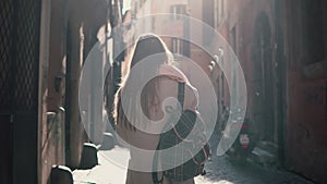 Back view of young woman walking at city street in Europe at morning. Girl exploring the old town alone, looking around.
