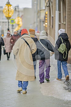 Back view of young woman walking at city street in winter. Modern city