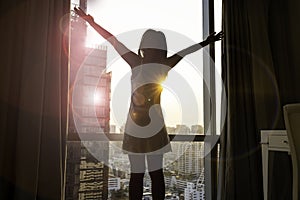 Back view young woman which she is looking at dawn city scenery  and stretch the muscles at window. Health