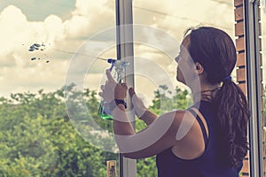 Back view of the young woman who washing the window with rag and window cleaner in the room. Cute girl with long hair washes a