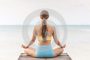 Back of views woman practice yoga lotus pose to meditation summer vacation on pier with sea beach