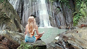 Back of woman meditating at the beautiful waterfall in green tropical rain forest in Bali