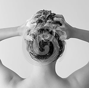 Back of a woman in a shower shampooing her hair, massaging her head full of suds in black and white.