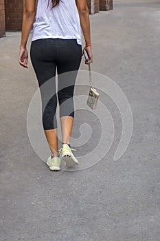 Back of a woman walking holding a hanging pocketbook in yoga pan