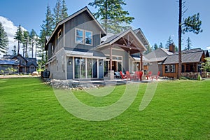 Back yard with fire pit and red chairs near newly bild luxury real estate home with forest biew and green grass