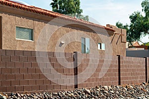 Back yard wall with red bricks and rock garden near sidewalk with orange stucco cement house with adobe roof tiles