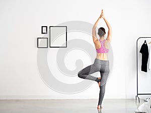 Back of Young beautiful caucasian sporty and active woman in sporty wear doing yoga position and meditating at home in white room