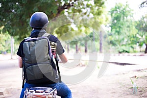 Back of Young happy and handsome male motorcyclist in helmet riding on motorbike on country road.