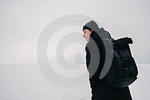 Back young man with a black backpack, traveling on snow-covered winter places