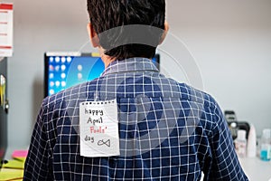 Back of young man office with a white paper note attached with the text happy april fools day