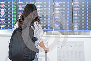 Back of young woman traveler with backpack and looking at departure board in airport terminal