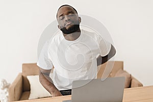 Backache. African american man suffering from low back pain from strenuous work on laptop while sitting at workplace in