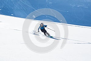 Backcountry skier on fresh powder slope in Alaska. Roller-balls fall behind him from steep cliff above