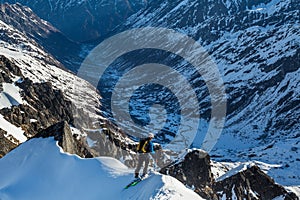 Backcountry skier peering over the steep edge of a summit ridge into the Bartholf Creek drainage