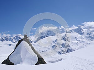 Backcountry skier sitting on top of a large snow-covered rock in midst of a spectacular winter mountain landscape