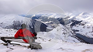 Backcountry skier takes a break and sit on a summit bench and enjoys the view of Davos in winter