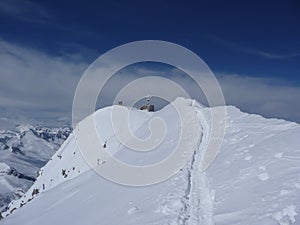 Backcountry skiers and mountain climbers stand near the summit cross of a high alpine moutnain peak in the Austrian Alps in deep w
