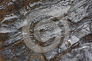 Background on the basis of the texture of rock. Black and brown stone with sloping layers and cracks