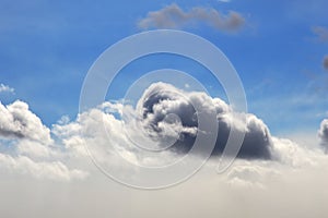 Background. Blue sky with a gray thundercloud in the middle, which dips into white feathery fluffy clouds. Fog rises from below.