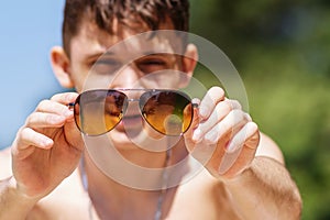 Background, blur, out of focus, bokeh. Portrait of a cheerful guy relaxing and having fun on a Sunny beach. Sunglasses in hand.