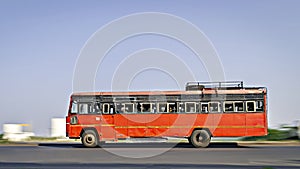Background blur, pan image of non air-conditioned red intercity bus in Maharashtra, speeding on the street