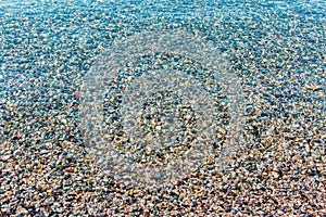 Background of blurred bright colorful sea stones under water. Iridescent sunlight on the stones. Clear water of sea