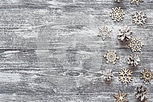 Background with a border of decorative wooden snowflakes and white painted pine cones on gray wooden table. Space for text.