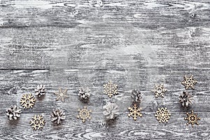 Background with a border of decorative wooden snowflakes and white painted pine cones on gray wooden table. Space for text.