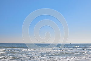 Background, clear blue sky, sea, waves crashing on the shore, seagulls flying low over the sea
