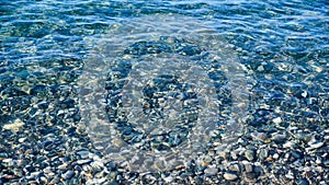 Background of clear blue water and pebbles under water, panoramic view