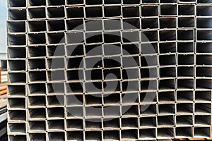 Background close up metal square pipes in stock. Stacks of new square steel pipes at the factory