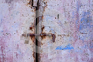 Background and close-up of an old weathered metal door that is secured with a metal latch