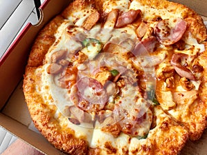 Background of close-up pizza with topping of hams, sausages and cheese in delivery box, ready to eat
