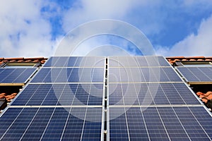 Background and close-up of a solar panel on a roof of a family home with red roof tiles, against a blue sky with clouds and