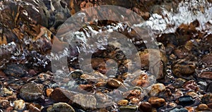 Background with colorful round sea pebble stones and foam on the shore. Banner.