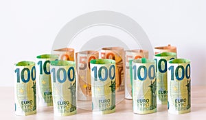 A background consisting of paper money in denominations of 100 and 50 euros, folded into a roll, each bill one at a time