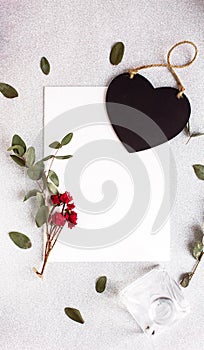 Background with copy space blank on table with black heart, eucalyptus branch, roses flowers and leafs. White paper top view, flat