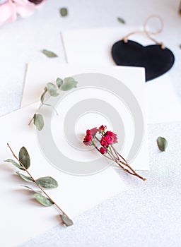 Background with copy space blank on table with black heart, eucalyptus branch, roses flowers and leafs. White paper top view, flat