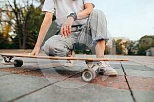 Background. Cropped close-up photo, a woman in street clothes sitting on the sidewalk with a longboard and resting. Women`s